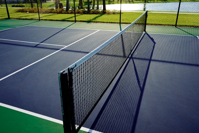 High-quality acrylic surface of a residential pickleball court installed by Liban Landscape, featuring black fencing and net.